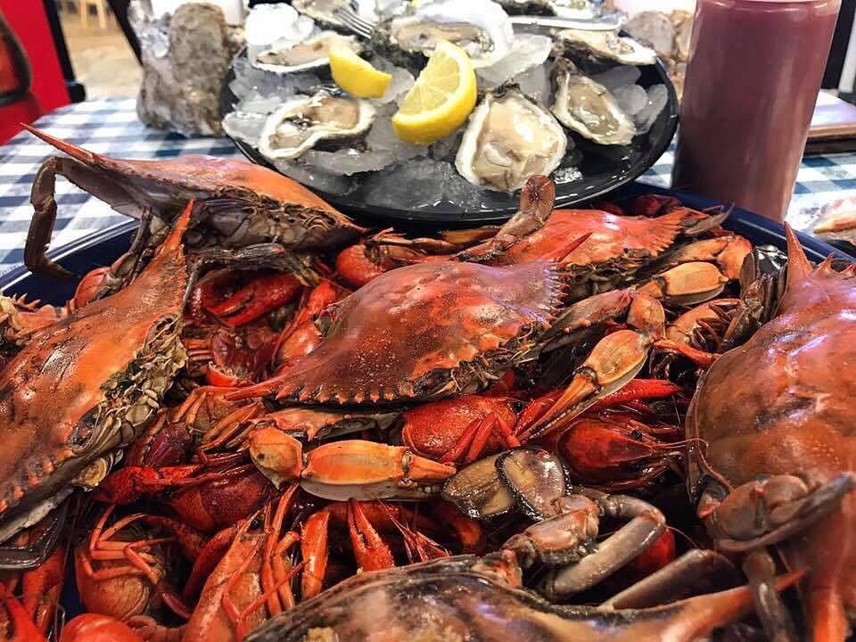 Boiled blue crabs and crawfish, with raw oysters on the half shell behind them.